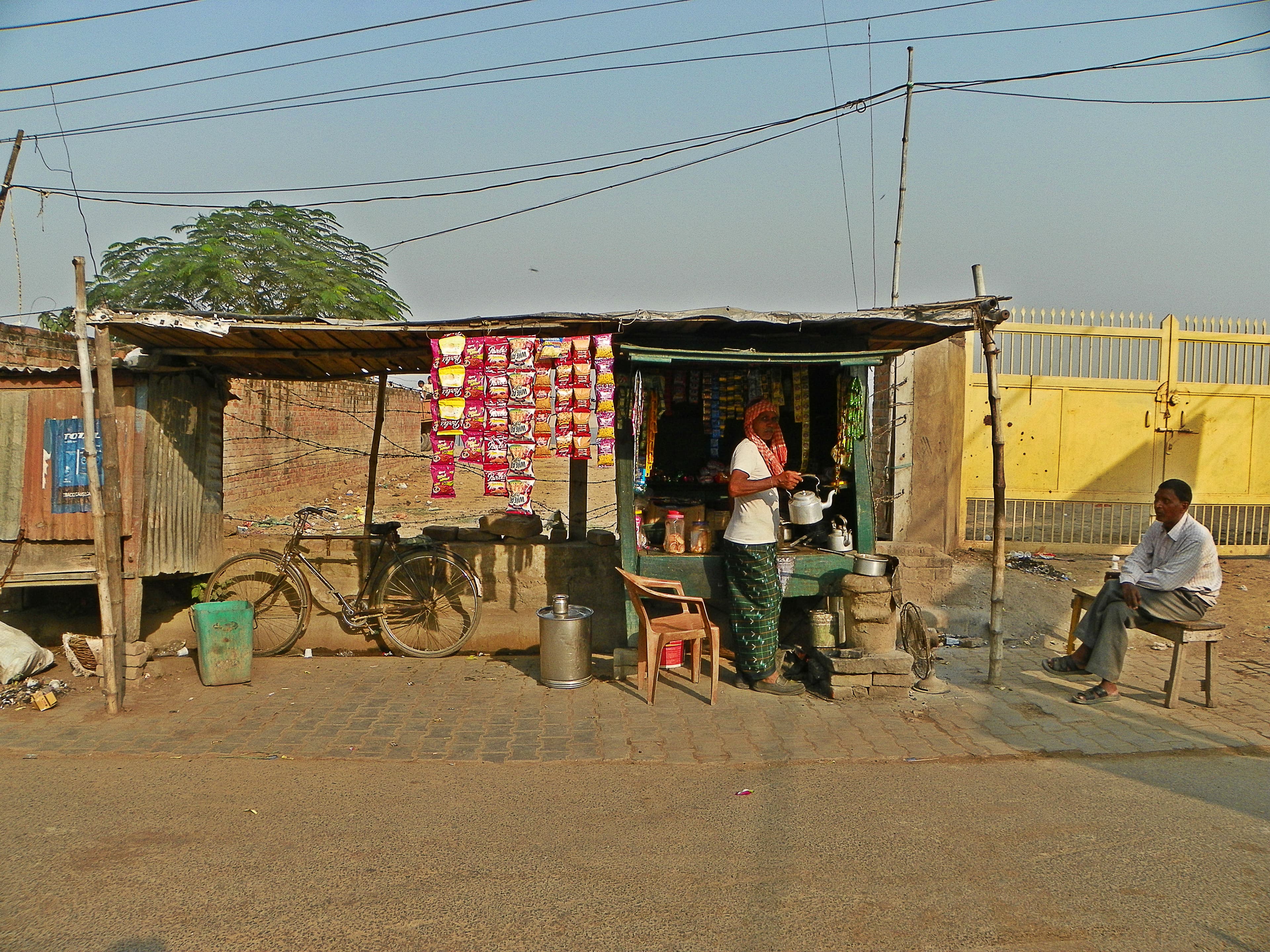 A small roadside dhaba stall in Varanasi — a woman cooking behind the counter, a man seated at a table outside.